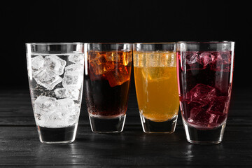 Refreshing soda water of different flavors with ice cubes in glasses on black wooden table