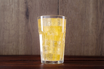Sweet soda water with ice cubes in glass on wooden table