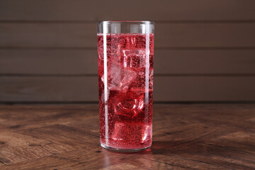 Sweet soda water with ice cubes in glass on wooden table
