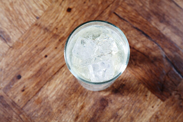 Refreshing soda water with ice cubes in glass on wooden table, top view