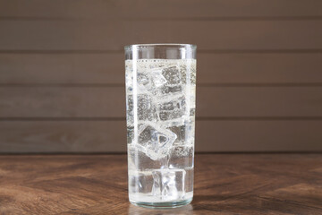 Refreshing soda water with ice cubes in glass on wooden table