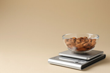 Electronic kitchen scale with almonds on beige background. Space for text