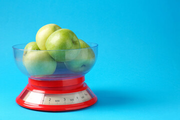 Kitchen scale with apples on light blue background, closeup. Space for text