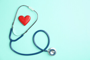 Fototapeta premium Cardiology. Stethoscope and red decorative heart on turquoise background, flat lay. Space for text