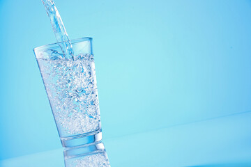 Pouring refreshing soda water into glass on light blue background, closeup. Space for text