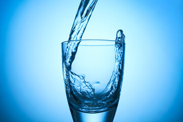 Pouring refreshing soda water into glass on light blue background, closeup