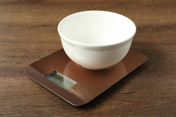 Modern electronic kitchen scale with bowl on wooden table, closeup