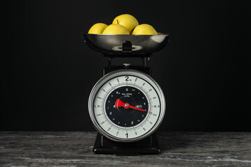 Mechanical kitchen scale with bowl of apples on dark textured table against black background