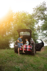 Father and child on outdoor adventure, sitting in car trunk in forest setting. Travel, family weekend, bonding and childhood memories.