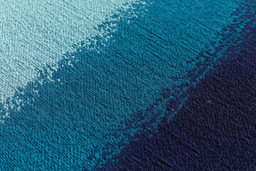 A close up shot of a textured fabric with a gradient of blues from light to dark in a diagonal pattern