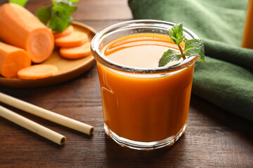 Fresh carrot juice in glass, vegetables, mint and straws on wooden table