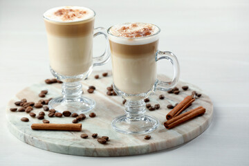 Tasty latte macchiato, coffee beans and cinnamon sticks on white table, closeup