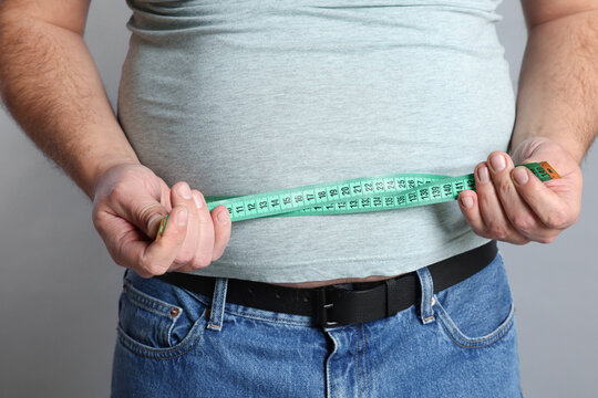 Overweight man measuring his belly with tape on grey background, closeup