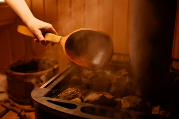 Woman pouring water on stones in sauna, closeup