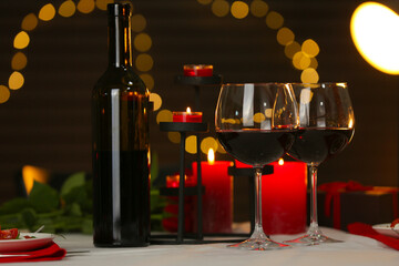 Romantic table setting with red wine and burning candles against blurred lights