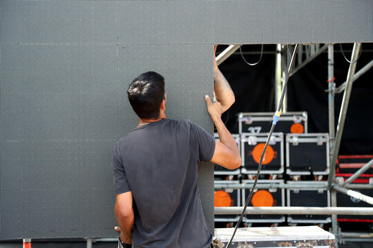 Technicians working on stage assembling giant LED screen panels for rock event. Men working on music show production	
