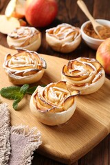 Tasty apple roses with powdered sugar served on wooden table, closeup