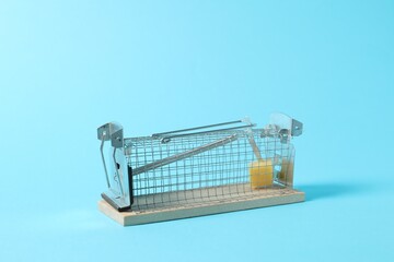 Metal mouse trap with piece of cheese on light blue background