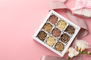 Flower shaped chocolate bonbons in box, gift, flowers and ribbon on pink background, flat lay. Space for text