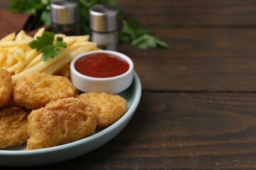Tasty chicken nuggets and french fries with sauce on wooden table, closeup. Space for text