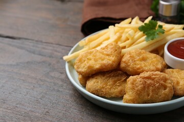 Tasty chicken nuggets and french fries with sauce on wooden table, closeup. Space for text