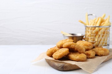 Tasty chicken nuggets, potato fries and sauce on white tiled table, closeup. Space for text