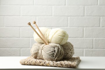 Skeins of yarn, knitted fabric and knitting needles on white wooden table