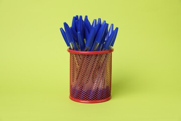 Many ballpoint pens in holder on green background