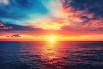 Obraz premium Dramatic sunset over a vast ocean. A vibrant, colorful sky with clouds of red, orange, and blue hues meet the horizon. The ocean's surface reflects the fiery colors of the setting sun