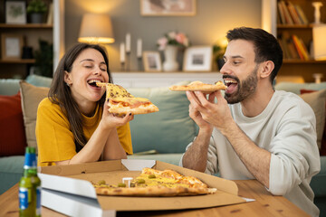 A joyful couple shares pizza slices, embodying togetherness and laughter in a warm, inviting living room setting.