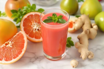 Fresh grapefruit juice with mint garnished in glass surrounded by ginger and whole fruits.
