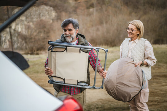 mature woman and man hikers pack equipment into the trunk of a car