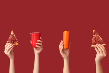 Many hands holding tasty pizza slices, one-use cup and can of soda on red background