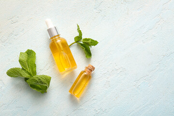 Bottles of essential mint oil and green leaves on pale blue background