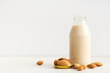 Bottle of fresh almond milk and nuts on white background