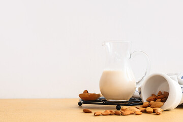 Jug of fresh almond milk and nuts on beige table