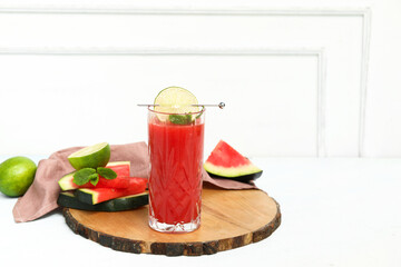 Glass of fresh watermelon juice with lime and mint on light blue table
