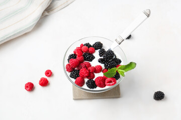 Glass bowl of tasty yogurt with fresh blackberries and raspberries on white background
