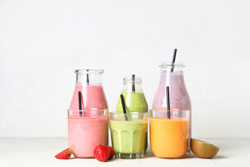 Glasses and bottles of different fresh smoothie with strawberries and kiwi on white background
