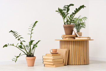 Round table, books, cup and different houseplants near white wall in living room