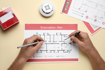 Man with smoke detector and fire call point drawing evacuation plan on yellow background