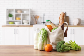 Grocery bag with different fresh products on wooden table in kitchen