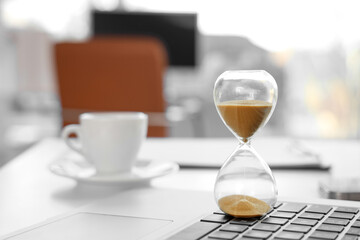 Hourglass on laptop in office, closeup