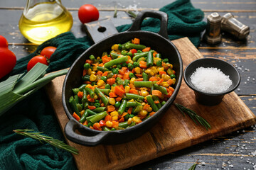 Frying pan with tasty roasted vegetables on black wooden background