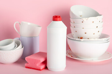 Dirty dishes, detergent and sponge on pink background