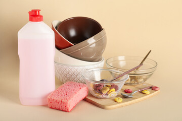 Dirty dishes, pink detergent and sponge on beige background