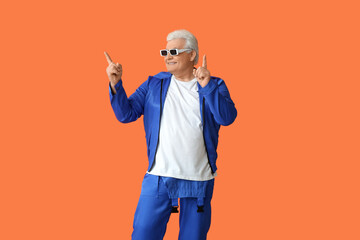 Happy stylish elderly man in sunglasses pointing at something on orange background. National Grandpa Day