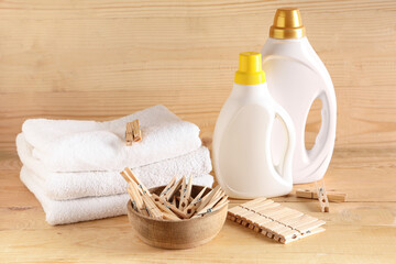 Bowl of clothespins with detergents and clean towels on brown wooden background