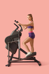 Fototapeta premium Sporty young woman training on modern exercising bike against pink background