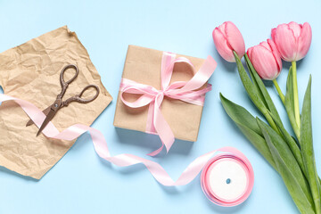 Gift box with tulips, wrapping paper and ribbon on blue background. International Women's Day